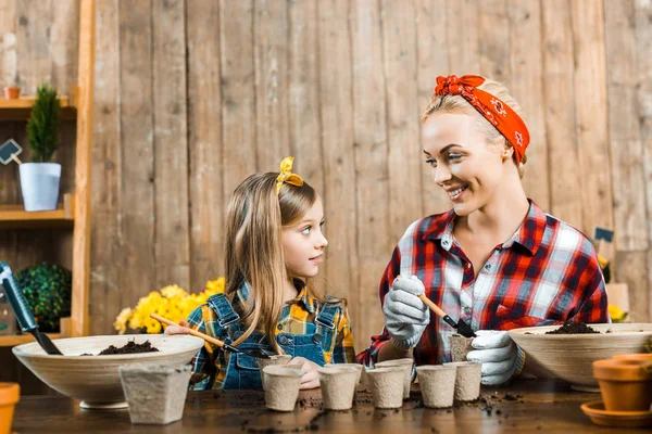 Cheerful mother holding small shovel with ground and looking at cute daughter — Stock Photo