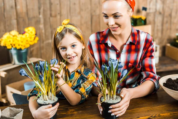 Madre feliz mirando a la hija y sosteniendo la olla con flores - foto de stock