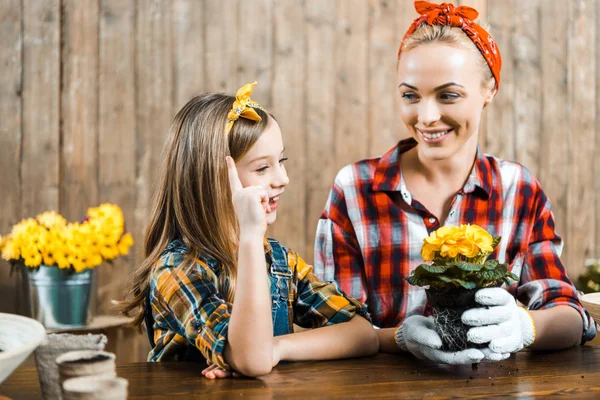 Enfant joyeux pointant du doigt près de mère heureuse tenant pot avec des fleurs dans les mains — Photo de stock