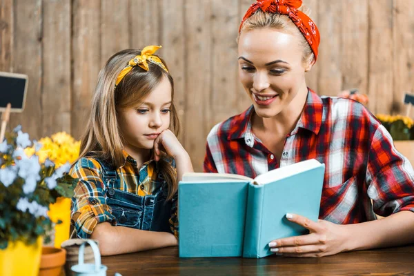 Cheerful mother reading book to cute daughter — Stock Photo
