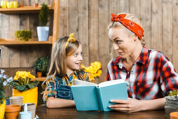 Allegra madre guardando la figlia carina mentre tiene il libro — Foto stock