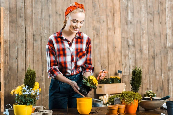 Donna felice in piedi vicino al tavolo e trapiantare fiori in vaso — Foto stock