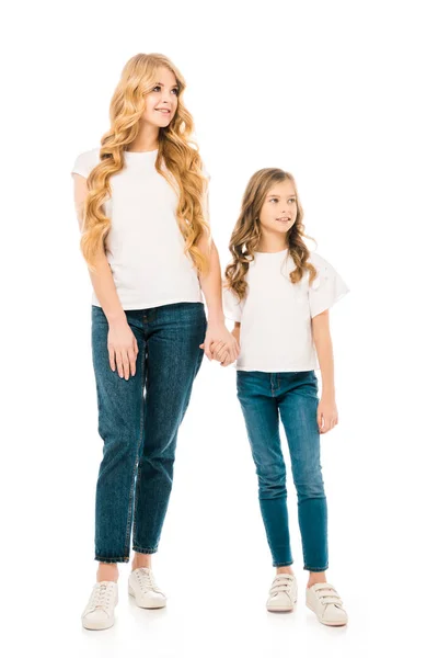 Mãe sorridente e filha adorável em camisetas brancas e jeans azuis de mãos dadas isoladas em branco — Fotografia de Stock