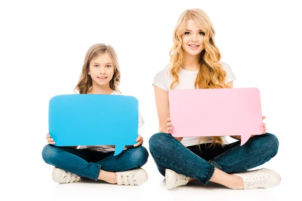 Cute child and beautiful mother sitting on floor with crossed legs and holding speech bubbles on white background — Stock Photo