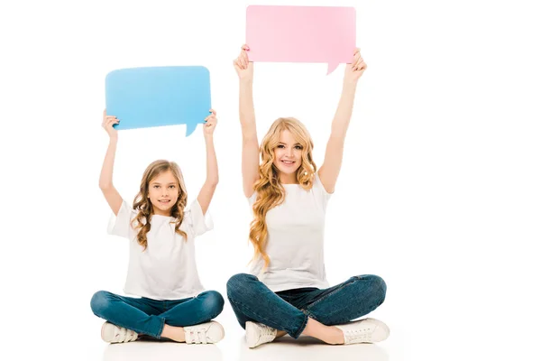 Adorable niño y bonita madre sentado en el suelo con las piernas cruzadas y la celebración de burbujas de habla en las manos levantadas sobre fondo blanco - foto de stock