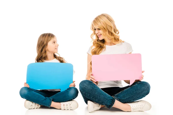 Beautiful woman with adorable daughter looking at each other while sitting on floor and holding speech bubbles on white background — Stock Photo
