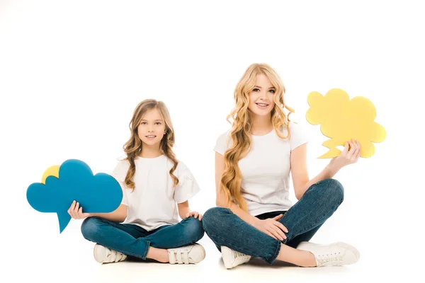 Sorridente mãe e filha sentado no chão com pernas cruzadas e segurando bolhas de fala no fundo branco — Fotografia de Stock