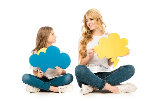 Beautiful woman with adorable daughter looking at each other while sitting on floor and holding thought bubbles on white background — Stock Photo