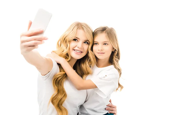 Lächelnde Mutter macht Selfie, während sie ihre entzückende Tochter isoliert auf Weiß umarmt — Stockfoto