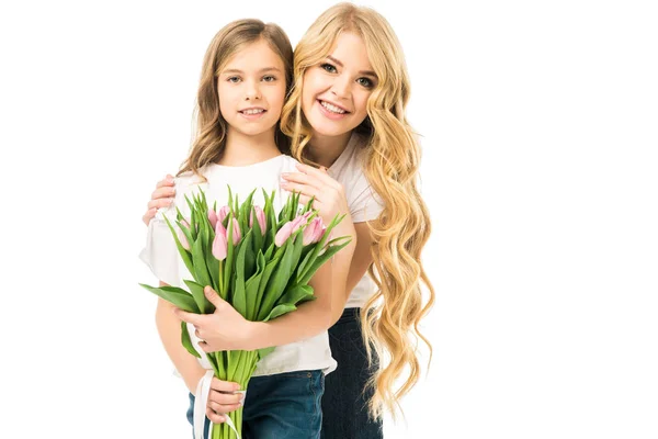 Feliz madre abrazando adorable hija sosteniendo ramo de tulipanes rosados aislados en blanco - foto de stock