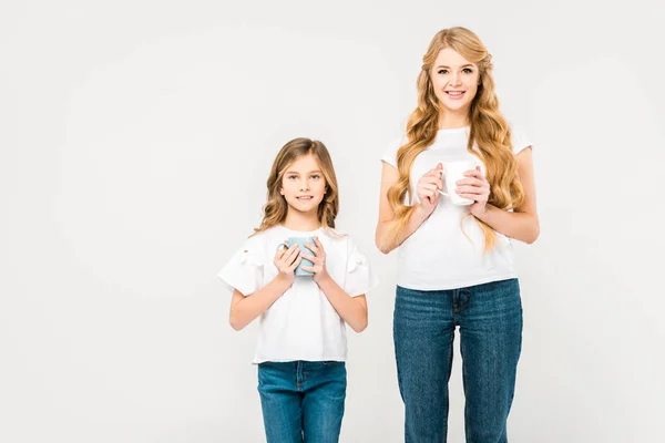 Улыбающаяся мать и милый ребенок держа чашки кофе на белом фоне — стоковое фото
