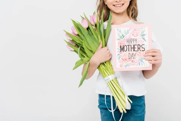 Vista recortada de niño sosteniendo feliz día de las madres tarjeta de felicitación y ramo de tulipanes rosados sobre fondo blanco - foto de stock