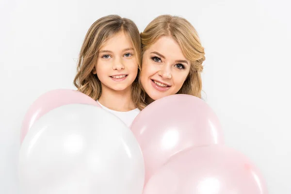 Maman et fille souriantes se cachant derrière des ballons à air blanc et rose sur fond blanc — Photo de stock
