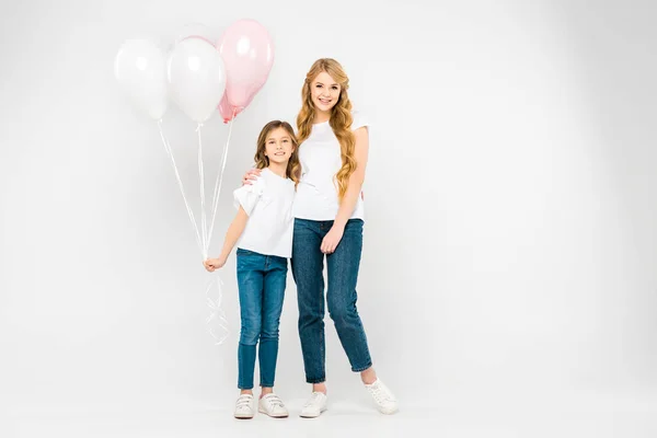 Mãe feliz abraçando adorável filha segurando balões de ar no fundo branco — Fotografia de Stock