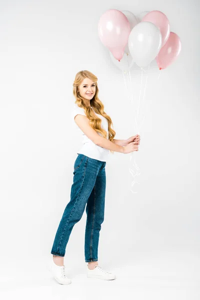 Attractive woman in white t-shirt and blue jeans holding festive air balloons on white background — Stock Photo