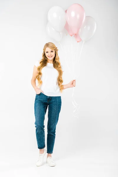 Lächelnde hübsche Frau mit der Hand in der Tasche, die Luftballons auf weißem Hintergrund hält — Stockfoto