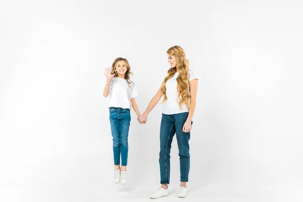 Happy daughter jumping and waving hand while holding mothers hand on white background — Stock Photo