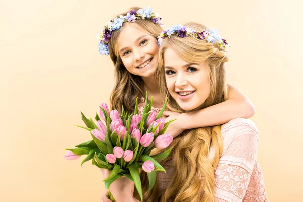 Beautiful woman and adorable daughter holding bouquet of pink tulips and looking at camera on yellow background — Stock Photo