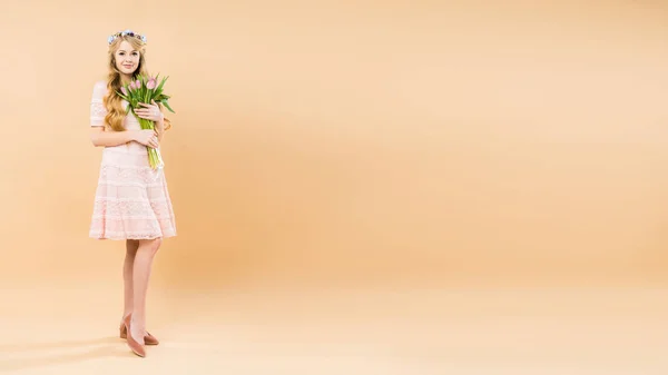 Jolie femme en délicate robe en dentelle et couronne florale tenant bouquet de tulipes roses sur fond jaune avec espace de copie — Photo de stock