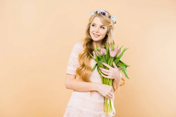 Femme souriante en robe de dentelle élégante et couronne florale tenant des tulipes roses et regardant loin sur fond jaune — Photo de stock