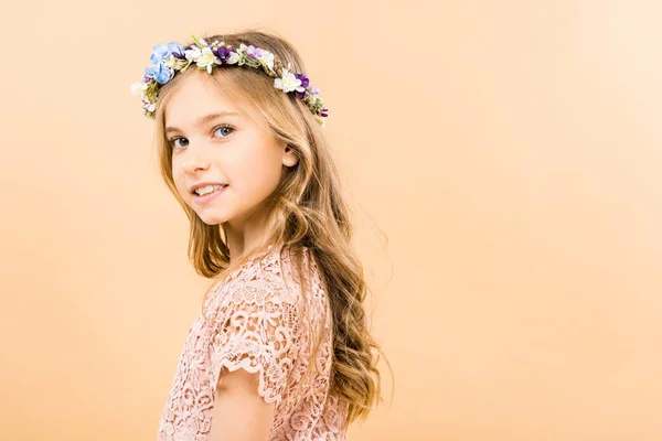 Adorable child in elegant lacy dress and floral wreath smiling and looking at camera on yellow background — Stock Photo