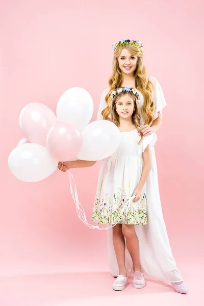 Adorable daughter holding festive air balloons while standing near beautiful mother on pink background — Stock Photo
