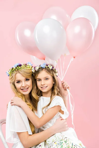 Happy mother sitting with adorable daughter and holding air balloons on pink background — Stock Photo