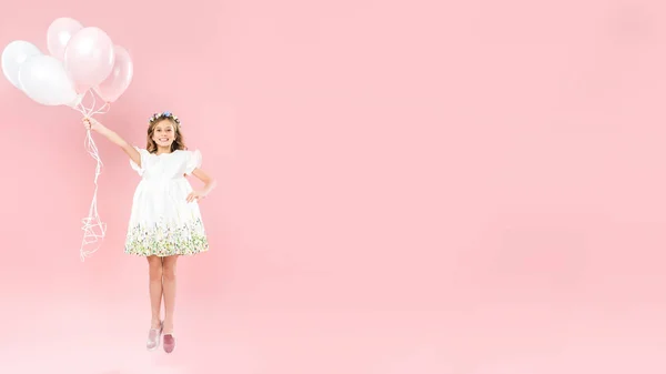Fröhliches Kind springt mit festlichen Luftballons auf rosa Hintergrund mit Kopierraum — Stockfoto