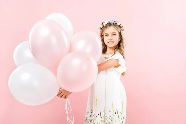 Adorable niño sonriente sosteniendo globos de aire festivos sobre fondo rosa - foto de stock