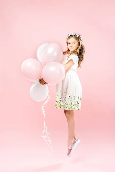 Cheerful child in delicate white dress jumping with air balloons on pink background — Stock Photo