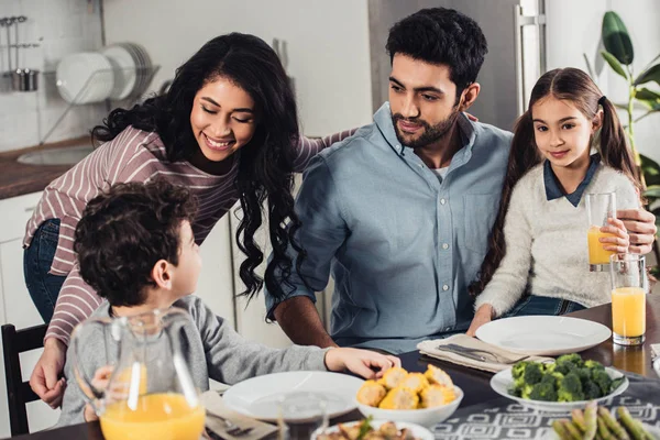 Cheerful latin woman looking at son near husband near daughter during lunch — Stock Photo