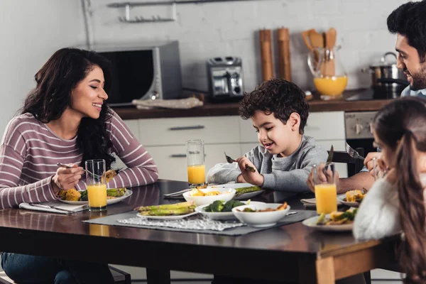 Heureuse mère latine regardant mignon fils ayant un déjeuner sain près de père et fille à la maison — Photo de stock