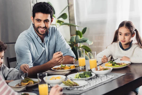 Guapo padre latino mirando esposa mientras almorza cerca de hija e hijo - foto de stock