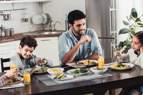 Handsome latin father looking at daughter while having lunch near wife and son — Stock Photo