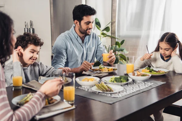 Enfoque selectivo de padre latino guapo mirando a la hija mientras almuerza cerca de la esposa y el hijo - foto de stock