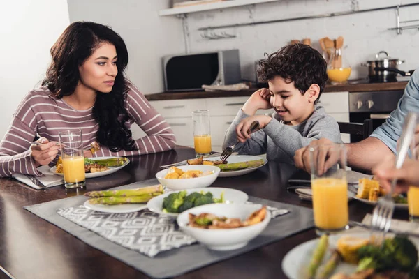 Selective focus of latin woman looking at cute son having lunch near father and daughter at home — Stock Photo