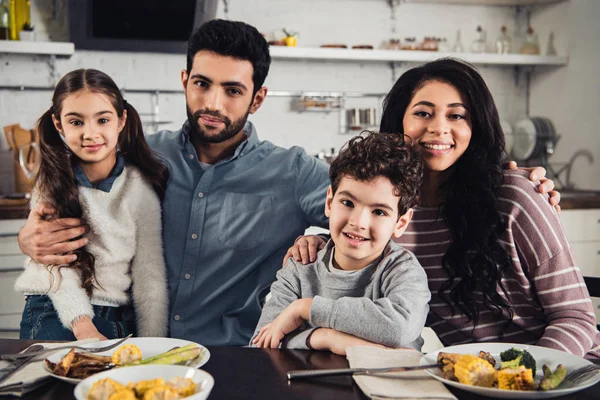 Joyeuse famille latino souriant tout en regardant la caméra pendant le déjeuner — Photo de stock