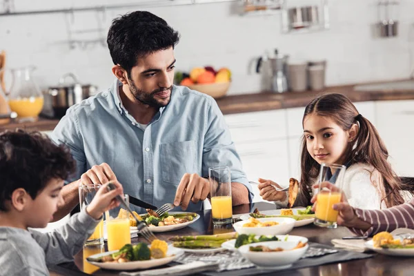 Handsome latin father looking at daughter while having lunch near son and wife — Stock Photo