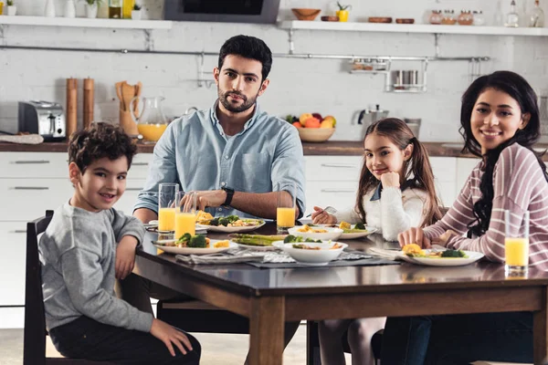 Alegre familia hispana sonriendo mientras almorzaba en casa - foto de stock