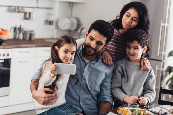 Niño latino alegre tomando selfie con la familia hispana en casa - foto de stock