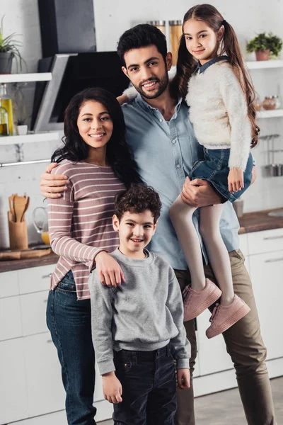 Guapo padre latino sosteniendo en brazos linda hija cerca de esposa e hijo en casa - foto de stock