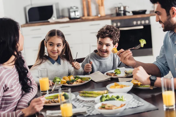 Lindos niños latinos mirando a la madre mientras almuerzan cerca de su padre en casa - foto de stock