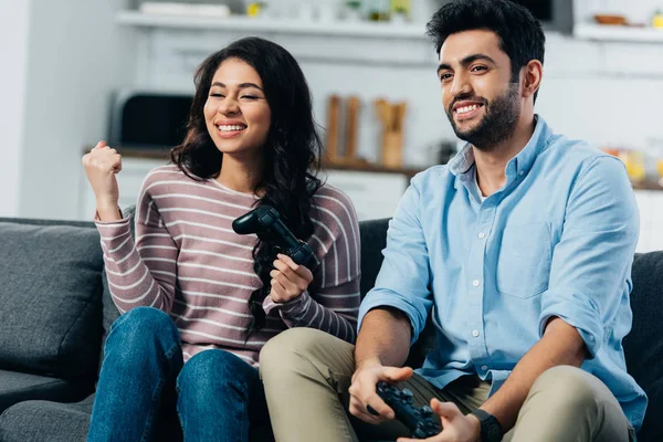 Fröhliche lateinamerikanische Frau feiert Sieg in der Nähe ihres Mannes beim Videospiel zu Hause — Stockfoto