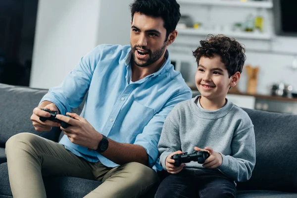 Feliz padre latino e hijo jugando videojuego en casa - foto de stock