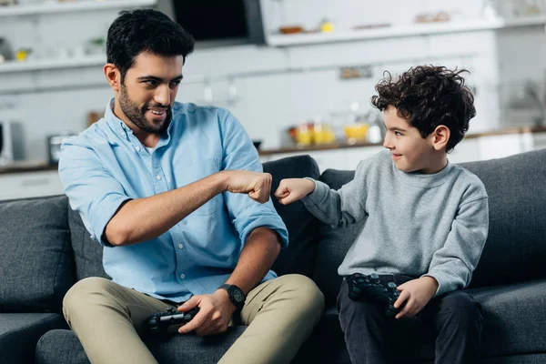 Cheerful latin father giving fist bump to son after playing video game at home — Stock Photo