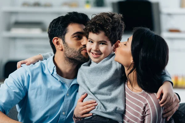 Happy latin father and mother kissing cheeks of cute son at home — Stock Photo