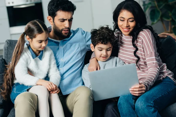 Allegra famiglia ispanica seduta sul divano e guardando il computer portatile a casa — Foto stock