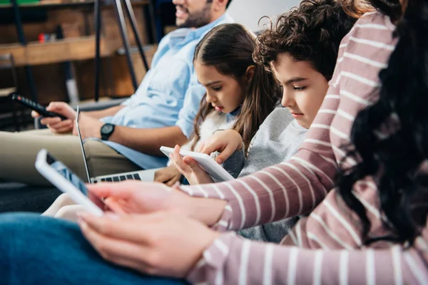 Selective focus of kids using gadgets near father and mother at home — Stock Photo