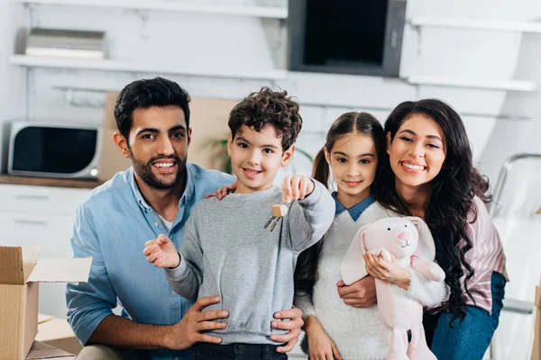 Cheerful latin kid holding keys from new home near happy hicpanic family — Stock Photo