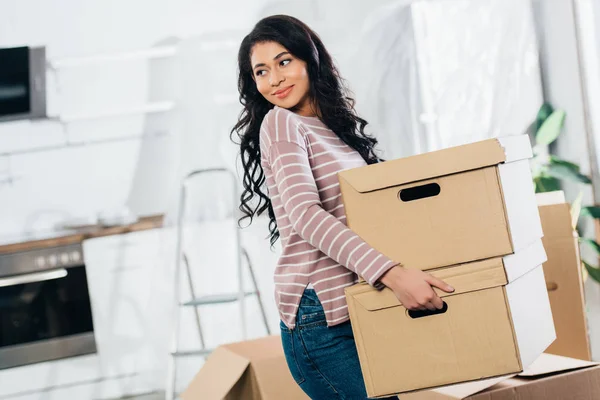 Happy latin woman holding boxes while moving in new home — Stock Photo